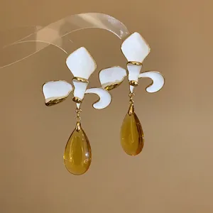 Detailed macro view of white enamel flower earrings with amber teardrop pendants in vintage style.