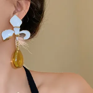 Close-up macro detail of white enamel flower earring with amber water drop pendant
