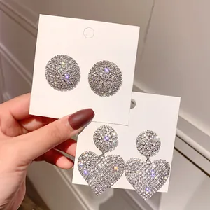 Macro view of sparkly rhinestone heart and circular earrings on white display cards
