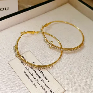 Primer plano de pendientes de aro dorados con strass pavé y detalle de cruz