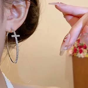 Primer plano de un aro de plata con cruz de diamantes brillantes puesto en la oreja