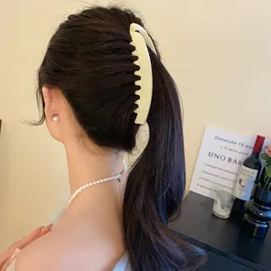 Gros plan d'une grande pince à cheveux en acrylique beige mat sur une queue de cheval.