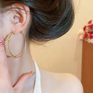 Detalle de aros grandes dorados con cruz de diamantes de imitación en modelo
