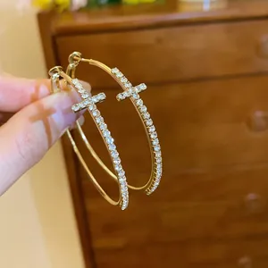 Primer plano de pendientes de aro con cruz bañados en oro y pedrería muy brillante