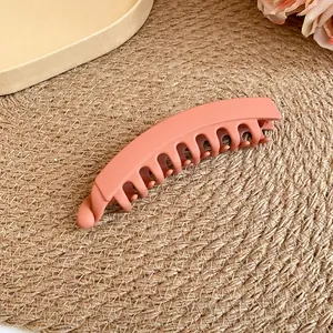 Gros plan d'une pince à cheveux banane rose mat montrant ses dents et sa texture lisse.