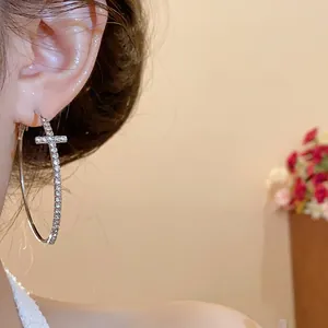 Primer plano detallado de aretes de aro plateados grandes con una cruz de diamantes falsos