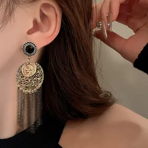 Close-up of vintage gold coin tassel earrings with black crystal stud and metal fringe.