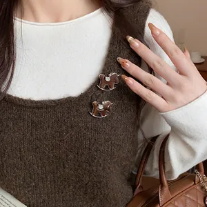 Detailed view of two flocked rocking horse brooches with rhinestones on a brown knit vest.