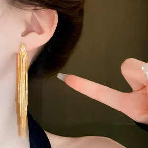 Detailed close-up view of elegant golden long metal tassel dangle earrings worn on ear