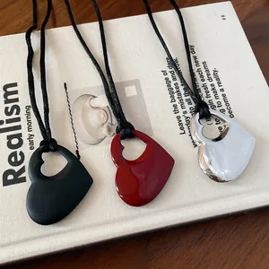 Gros plan de trois pendentifs tendance en forme de cœur évidé en noir, rouge et argent.