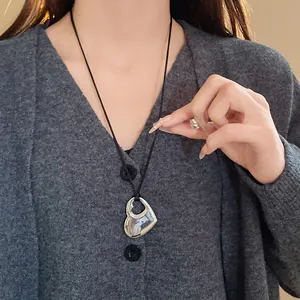 Gros plan d'un collier avec pendentif cœur ajouré minimaliste porté sur un pull gris.