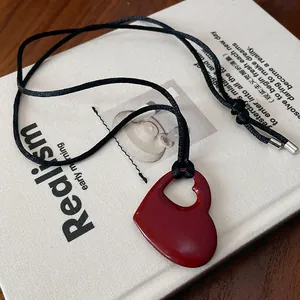 Gros plan d'un collier pendentif cœur rouge évidé sur le fond texturé d'un livre beige