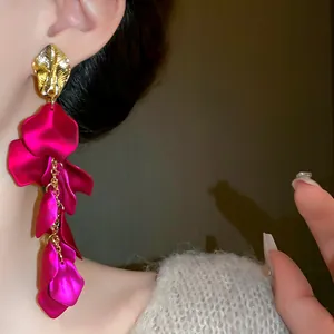 Primo piano di eleganti orecchini lunghi con nappe a petali fucsia e foglia dorata