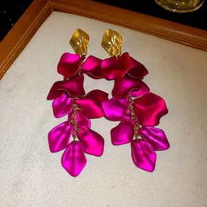 Primo piano dei dettagli di orecchini a petalo fucsia con perni a foglia dorata.