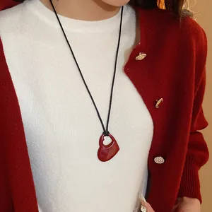 Gros plan d'un collier pendentif cœur rouge porté avec un cardigan rouge confortable.