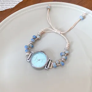 Elegant woven rope watch bracelet with blue ceramic beads on a white plate.