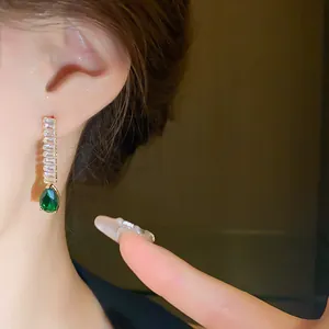Gros plan de boucles d'oreilles élégantes en goutte d'émeraude avec zircons baguette.