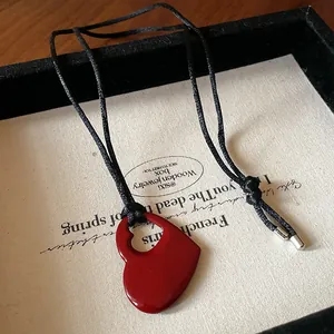 Gros plan sur un pendentif coeur rouge ajouré avec cordon noir dans une boîte cadeau.