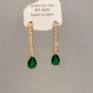 Détail de boucles d'oreilles dorées avec zircon vert en forme de poire et pierres