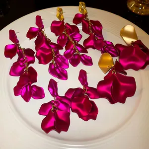 Dettaglio di orecchini a nappa con petali fucsia e borchie geometriche dorate lucide.