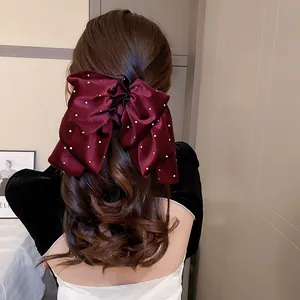 Eleganter weinroter Samt-Bogen-Haarclip mit Perlen auf langem lockigem Haar.