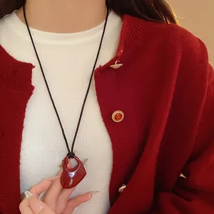 Détail d'un collier avec pendentif cœur rouge porté sur un tricot blanc et gilet rouge