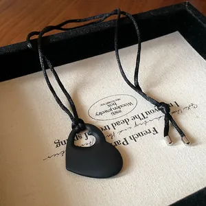 Détail d'un pendentif cœur creux noir mat sur un collier minimaliste en cordon noir