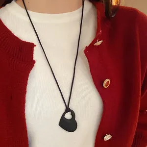 Gros plan d'un collier pendentif cœur évidé noir porté avec un cardigan rouge élégant
