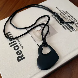 Gros plan d'un pendentif cœur creux noir mat minimaliste sur un cordon noir élégant.