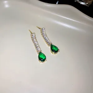 Gros plan de boucles d'oreilles dorées avec pierres vert émeraude en goutte et zircon.