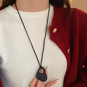 Détail en gros plan d'un collier pendentif cœur noir mat porté avec un pull d'hiver chaud