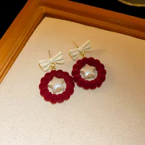 Close-up detail of red velvet bow earrings with a pearlescent star in a wooden frame