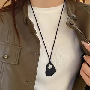 Gros plan d'un collier cœur noir mat porté avec une veste en cuir marron élégante