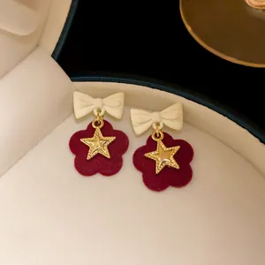 Macro view of sweet burgundy velvet flower earrings with gold stars and white bows