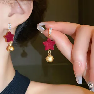 Macro view of Christmas red velvet star earrings with golden bell dangles worn on ear