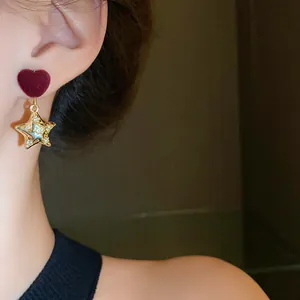 Detailed close-up of elegant velvet heart and gold star drop earrings worn on ear