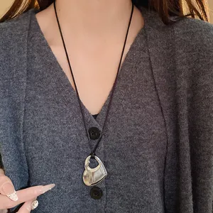 Détail d'un collier avec pendentif cœur ajouré argenté porté sur un cardigan gris