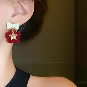 Close-up view of red velvet flower earrings with white bowknot and gold star charm