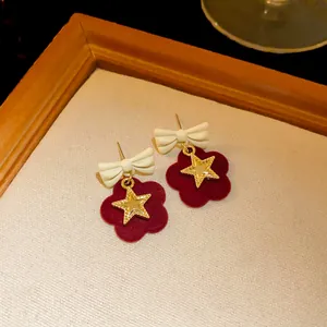 Detail view of velvet bow earrings with red flower and gold star charm
