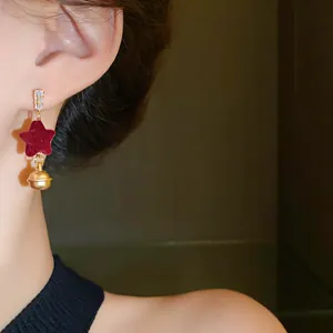 Detailed view of elegant Christmas red velvet star earrings with gold bell pendant on model