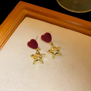 Detailed macro shot of burgundy velvet heart and gold star earrings with sparkling stones.