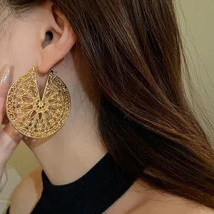 Gros plan de grandes boucles d'oreilles circulaires en filigrane d'or portées par un mannequin.