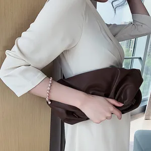 Elegant baroque freshwater pearl bracelet on a model's wrist with a brown clutch.