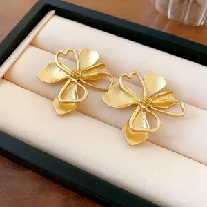 Detalle macro de pendientes de flores doradas con recortes de corazón en estuche