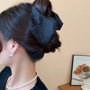 Elegant large black fabric bow hair claw clip styled on a classic hair bun hairstyle.