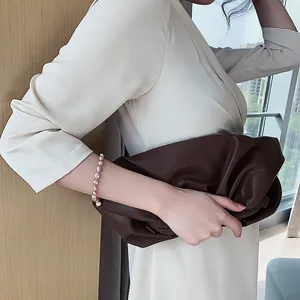 Elegant baroque freshwater pearl bracelet on wrist paired with a stylish brown clutch.