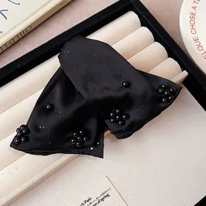 Macro detail of elegant black fabric hair claw clip featuring shimmering bead embellishments