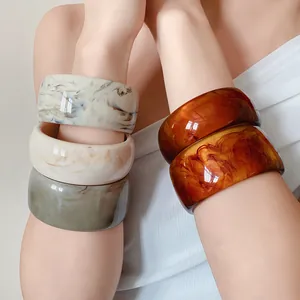 Detailed shot of stylish wide marbled resin bangles in multiple colors on a model's arm