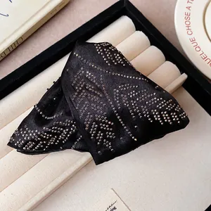 Close-up of a black satin triangular hair claw clip decorated with sparkling rhinestones.