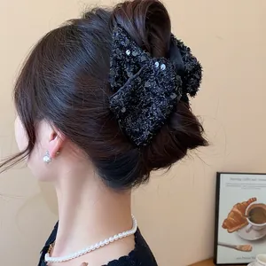 Close-up detail showing a large black sequin bow hair claw clip styled in an elegant bun